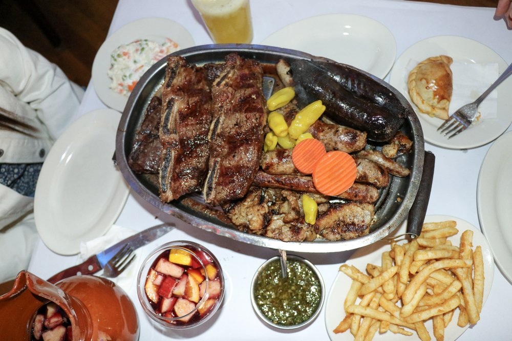 A platter of grilled meats on a table with small bowls for sauce.