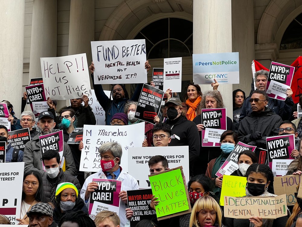 Protesters on the steps of City Hall holding signs opposing Mayor Adams' mental health directive.