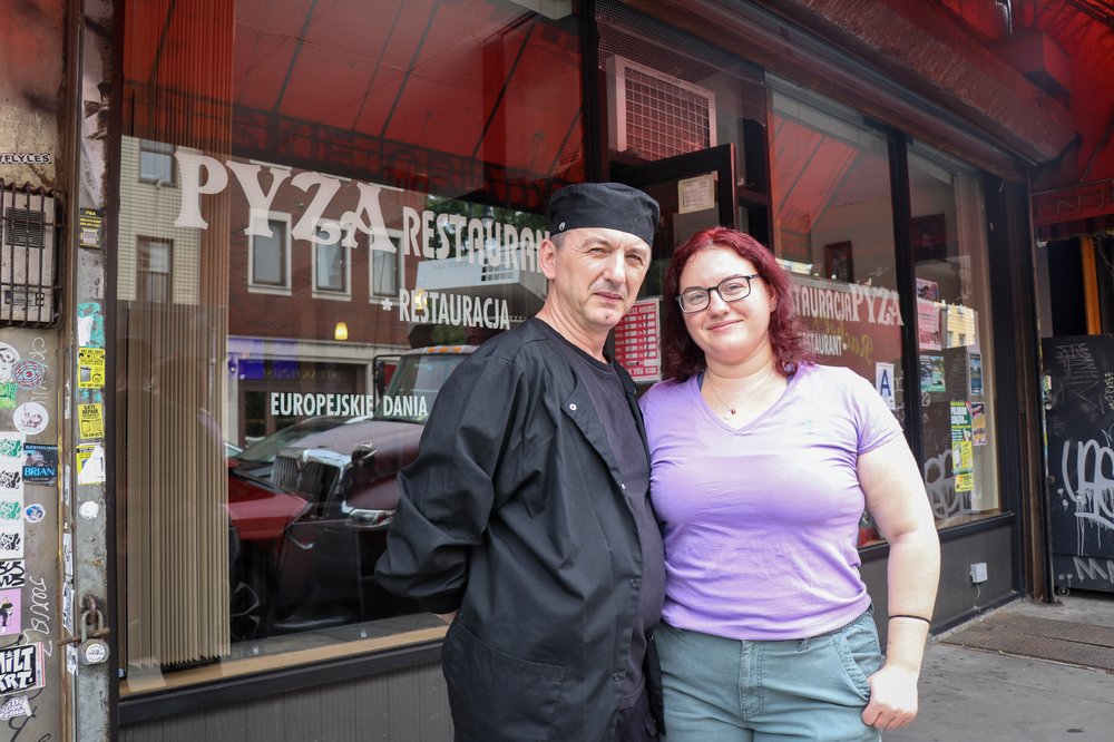 A man and a woman stand in front of a restaurant.