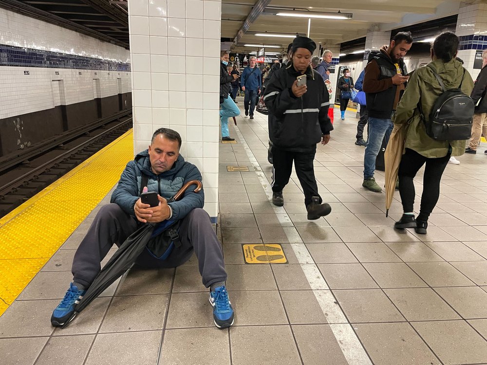 A dejected man sits on the platform of a Brooklyn subway station.