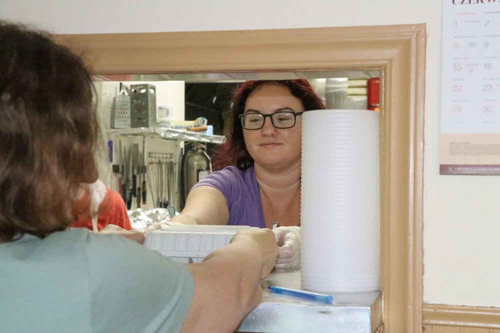 A woman pushes a plate of food through a takeout window.