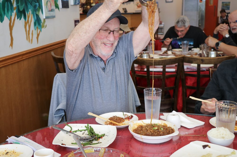 A man serves noodles onto a plate in a restaurant.