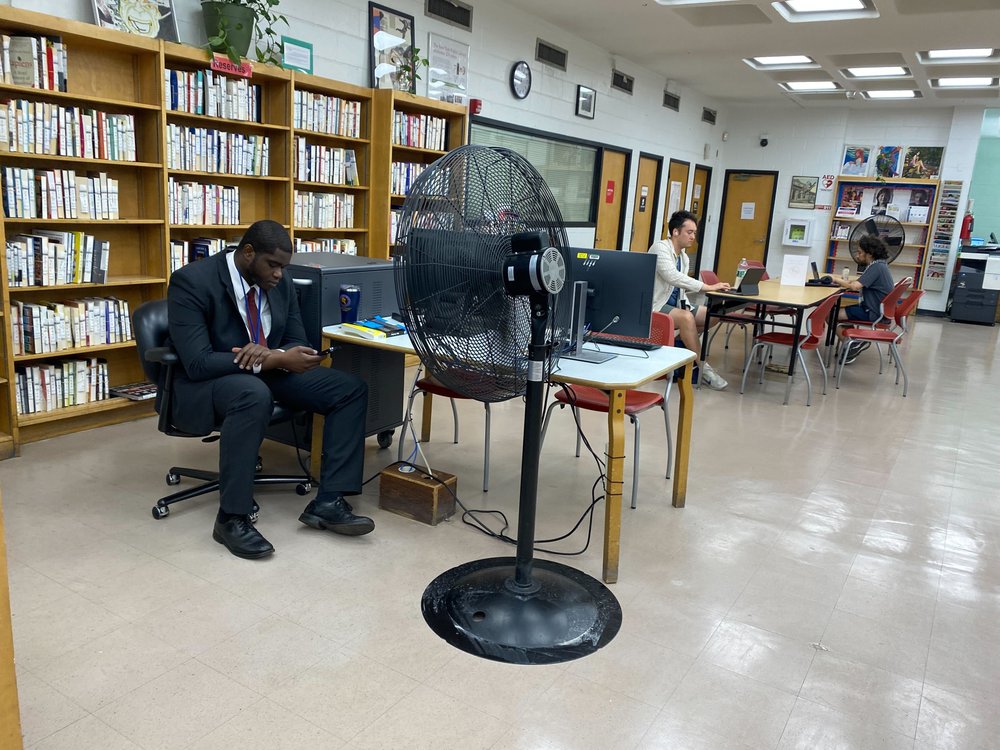 A security guard at the Kips Bay library branch sits in front of a large black fan.