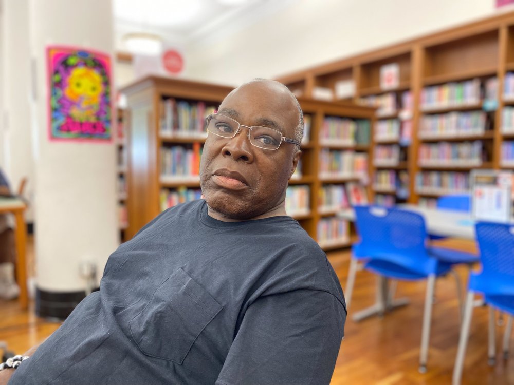Bobby Williams, in a black T-shirt, sits at a table inside the Tremont branch library.