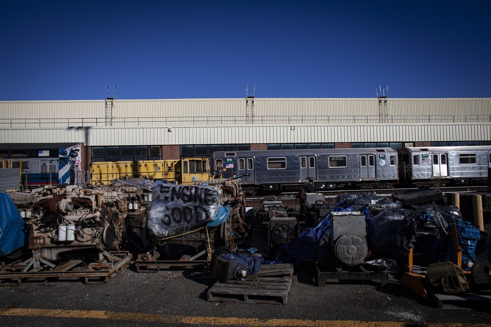 A depressing train yard. A subway car sits next to an old, rusted yellow work train. In the foreground, a piece of equipment is wrapped in plastic that says "Engine good." The word "good" is perhaps the only positive thing about this image. This shows an MTA yard in the Bronx where train equipment is repaired. But it's a hopeless place, in dire need of upgrades and repairs. The MTA hopes to upgrade the facility through its latest capital plan.