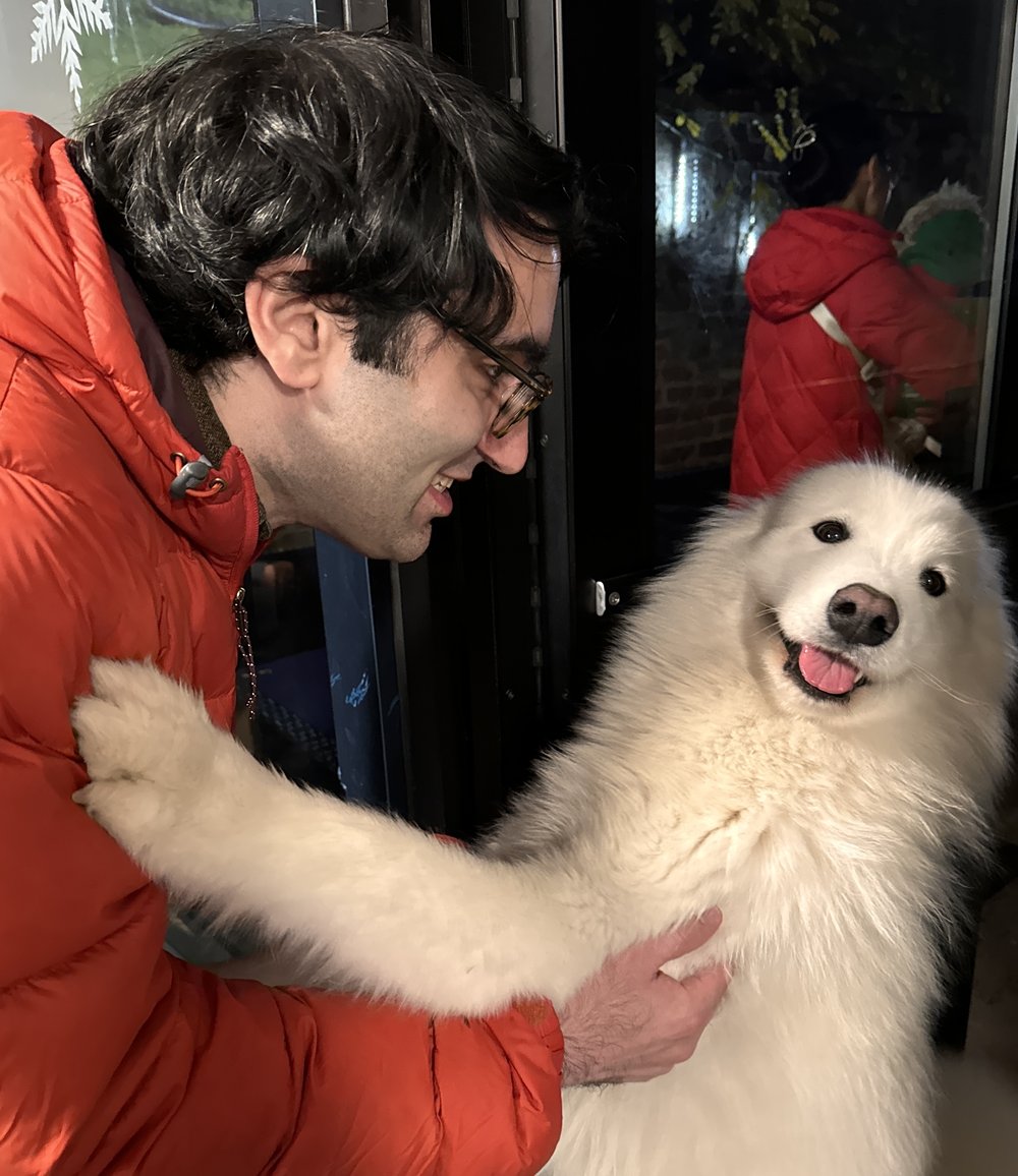 A man in a red parka hugs his fluffy white dog.
