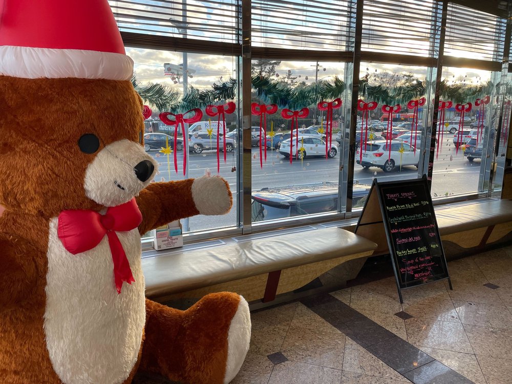 An animatronic teddy bear wearing a Santa hat and bow greets people at the entrance of the Carle Place Diner