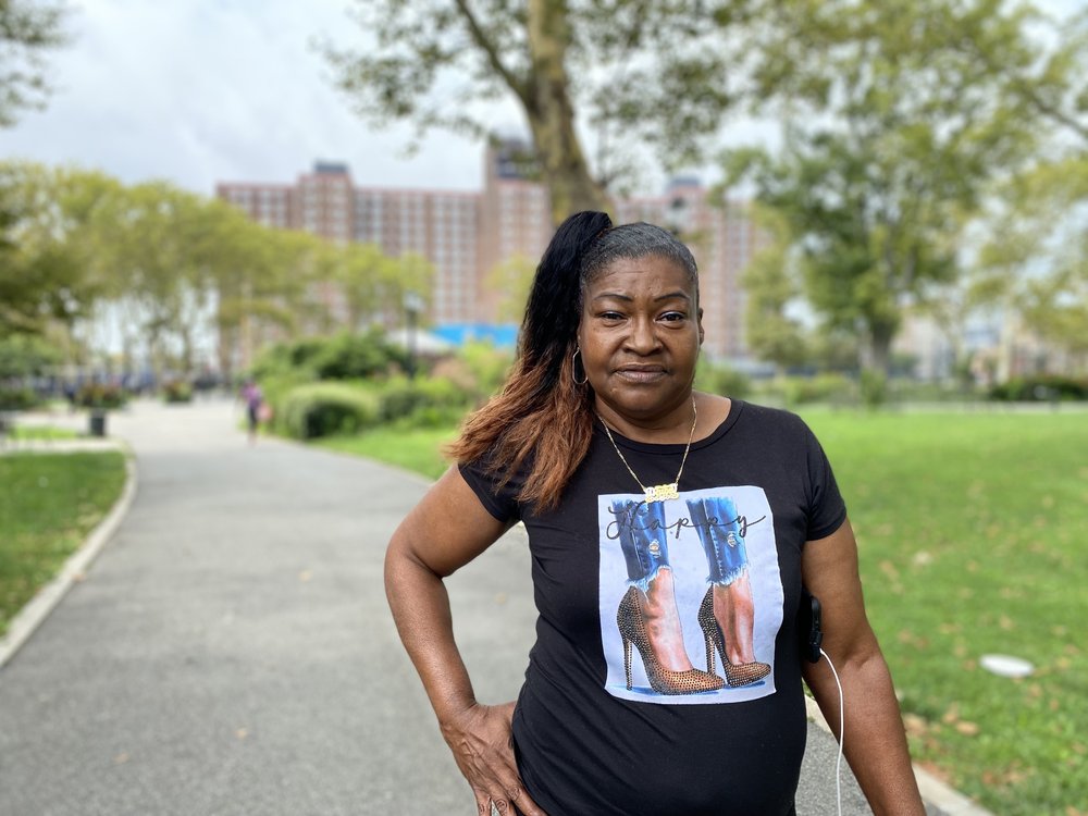 Karen Blondel, wearing a black t-shirt and high ponytail, stands in front of the Red Hook Houses in Brooklyn.