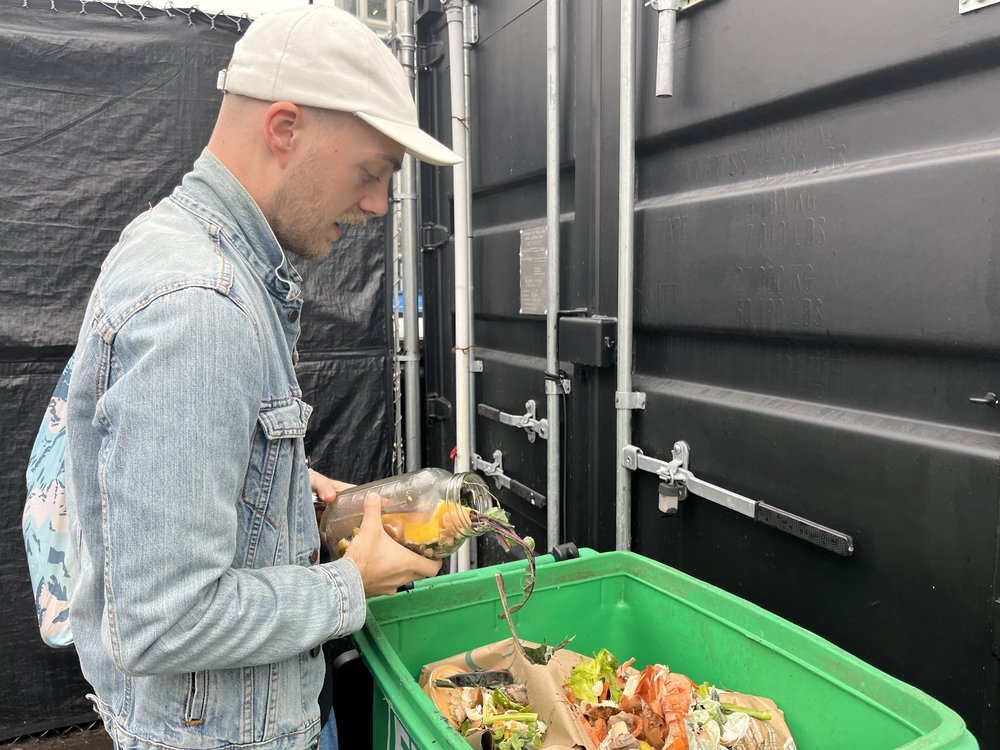 A man tosses food scraps into a green bin.