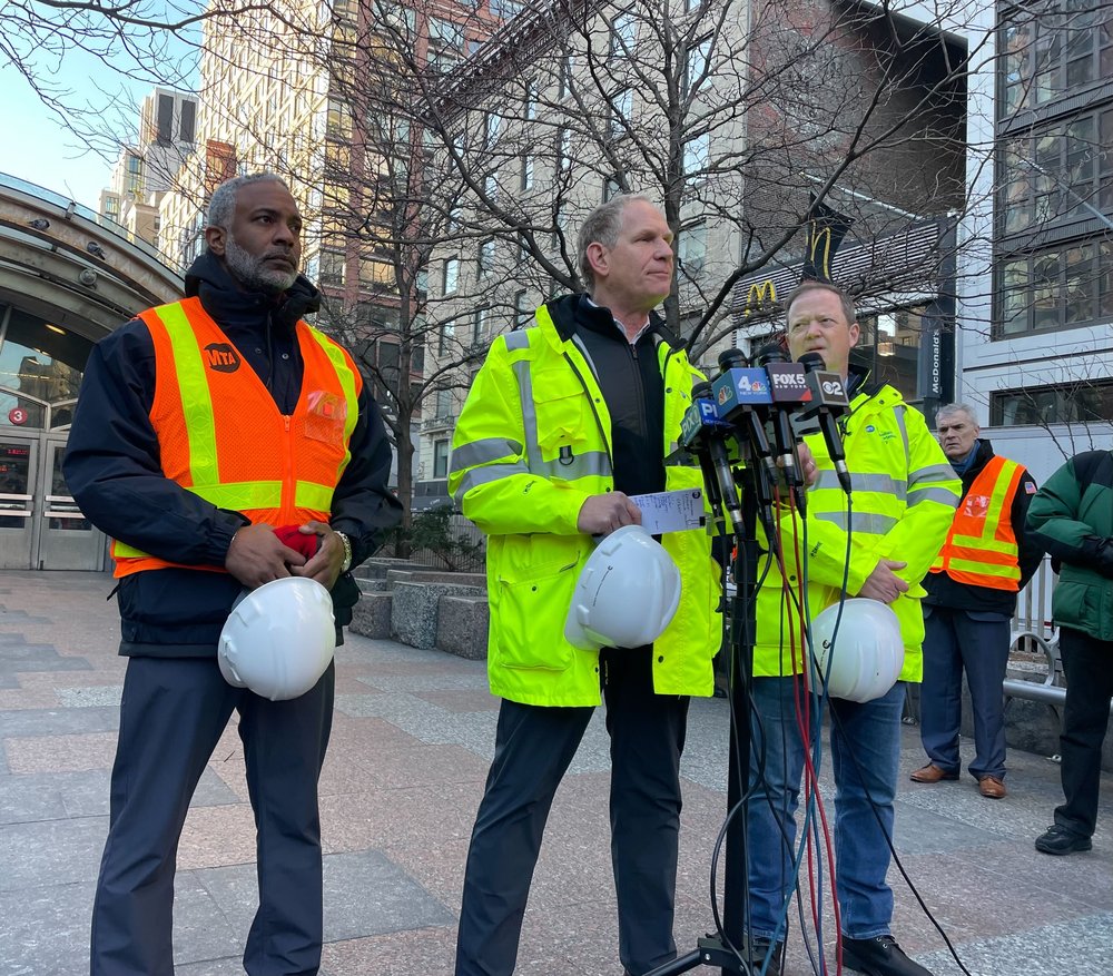 Transit officials in neon safety vests brief the press outside of the 96th Street Station.