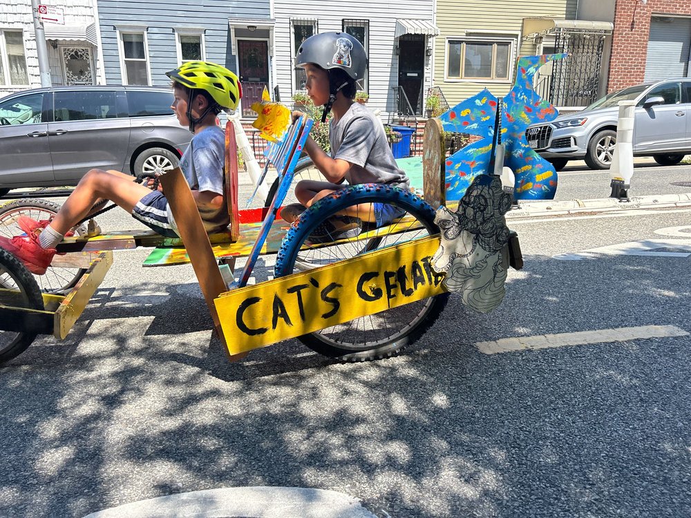 Two kids race a derby car with "Cat's Gelato" written on the side