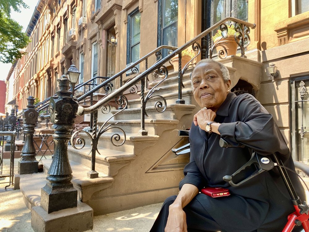 Frankie Scott sits next to the stairs of her Bed-Stuy brownstone home.