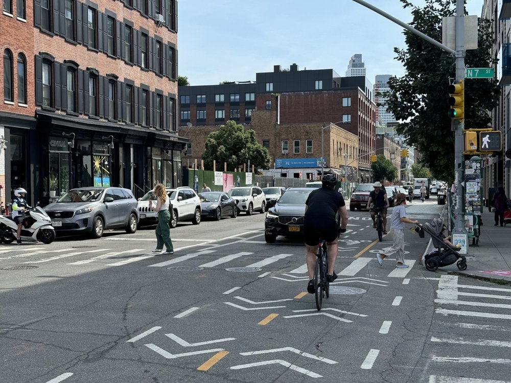 A cyclist in a bike lane, a mom pushing a stroller and a pedestrian.