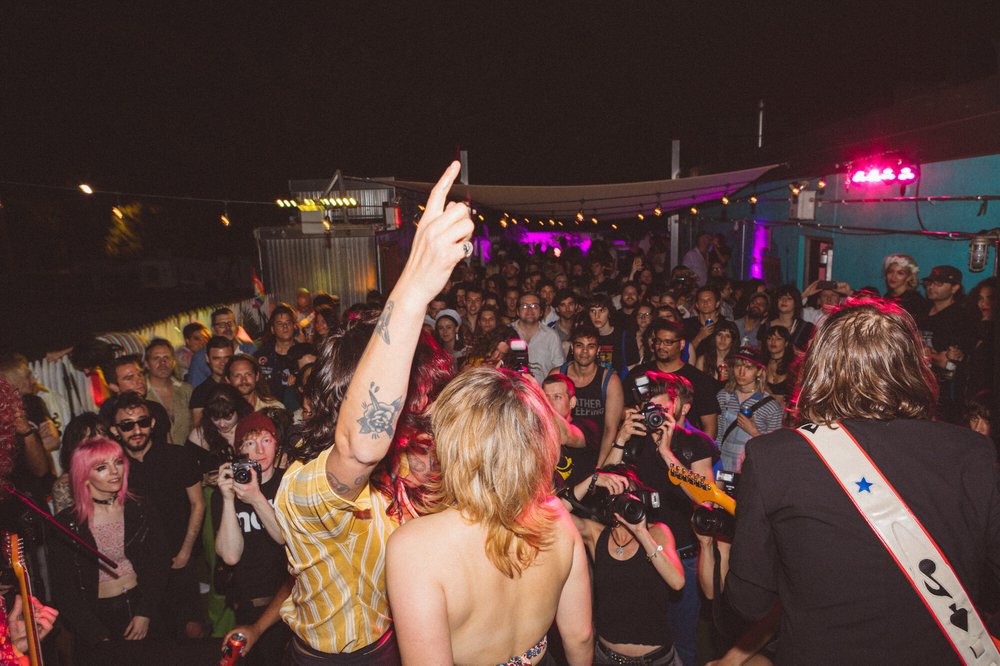 A person raises their hand in front of a crowd in a nigthclub.