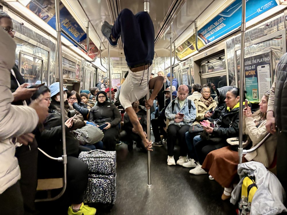 A man performing on a subway train, holding onto a pole, doing flips.