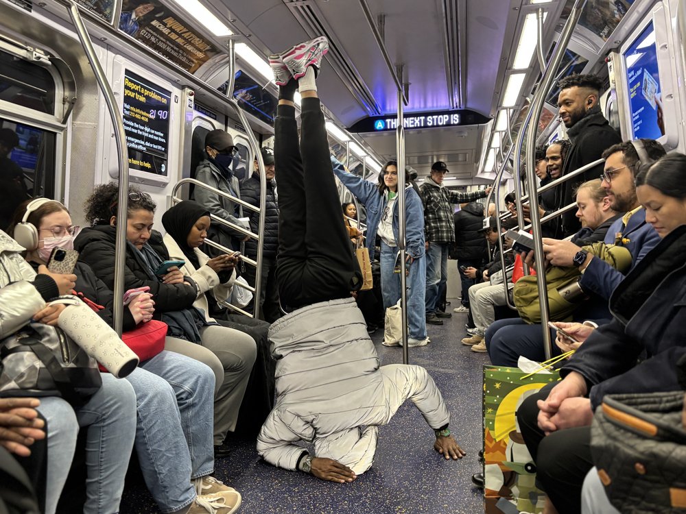 A man standing on his head on a subway car.