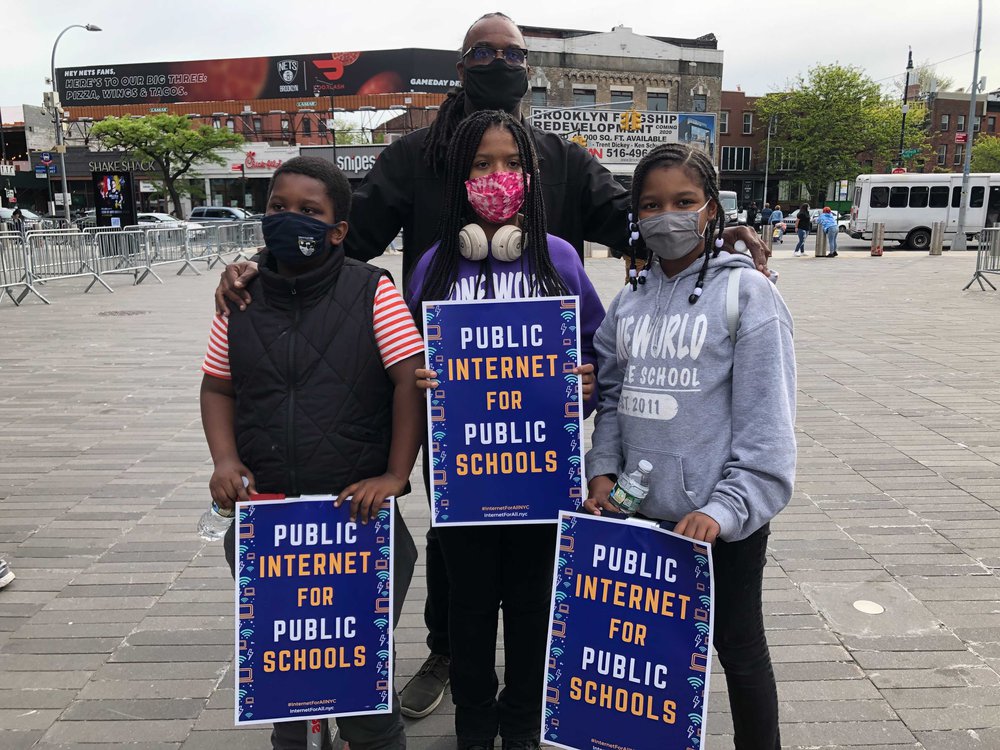 Tom Sheppard and his three children hold signs that say "Public Internet for Public Schools"