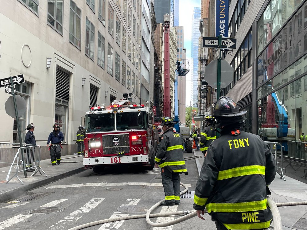 Firefighters stand on a New York City street. A fire truck can be seen in the background.