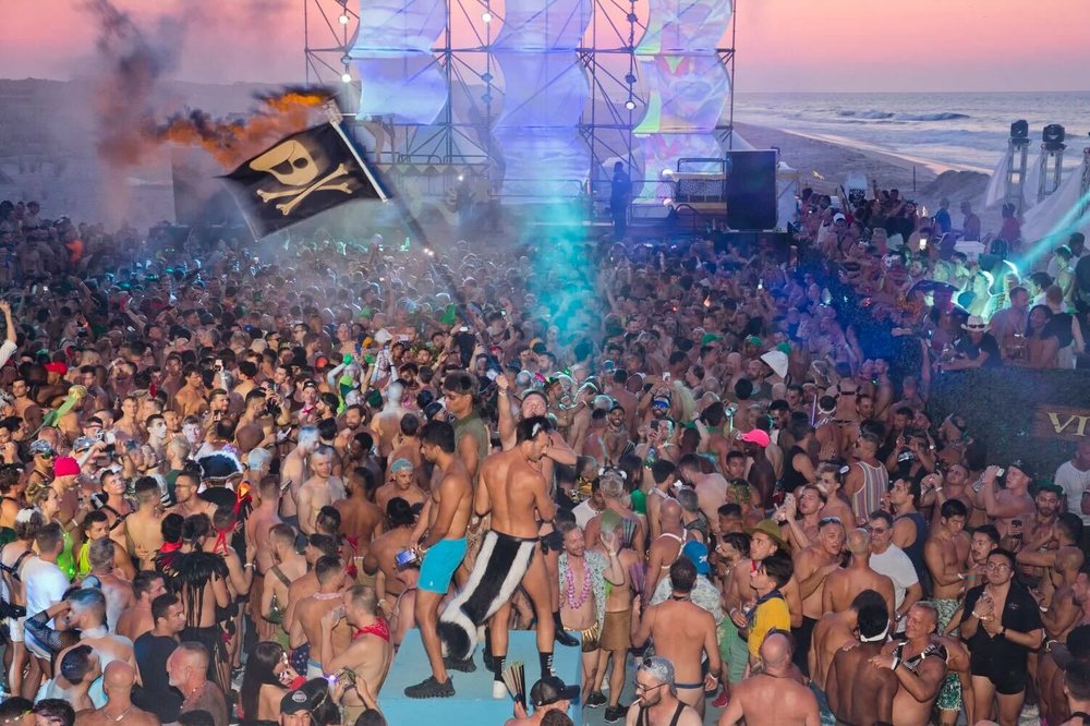 A crowd of partiers in front of a stage on a beach