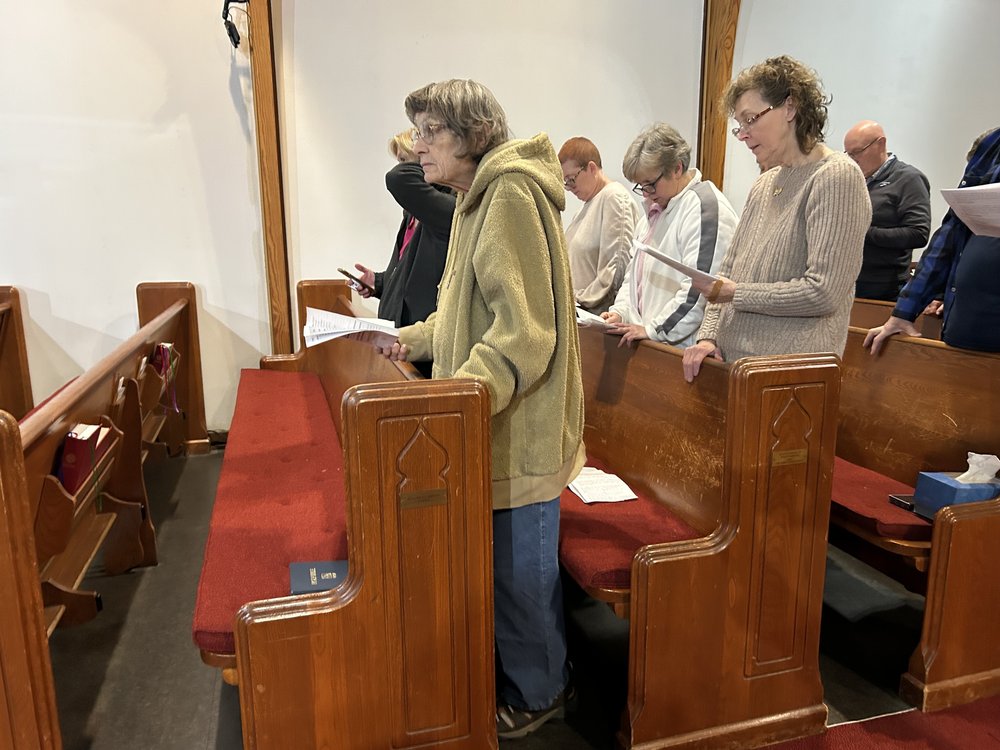 An elderly woman stands in the church pews.