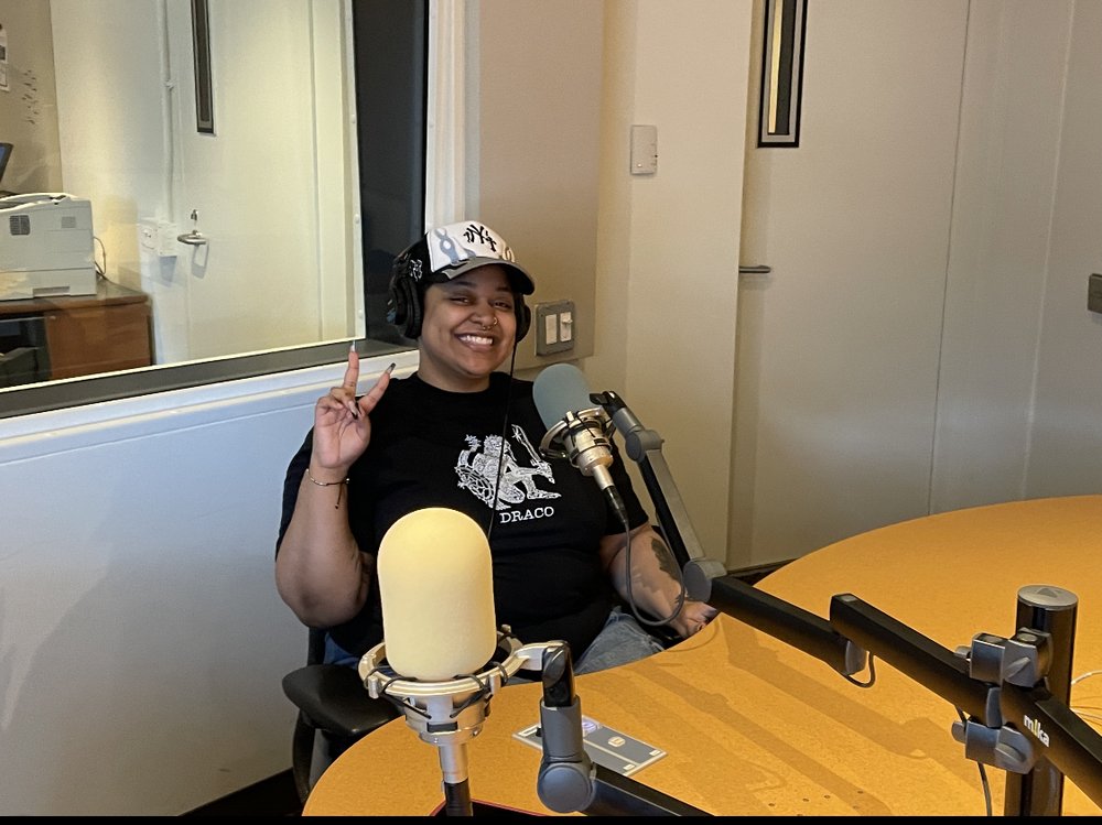 A woman seated in a studio facing a microphone.