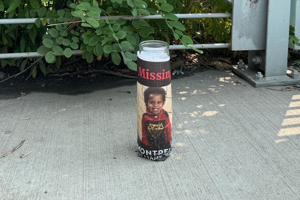 A lone candle bearing a photo of Montrell Williams stands near a cycling path in Garrison Park by the Bronx River.