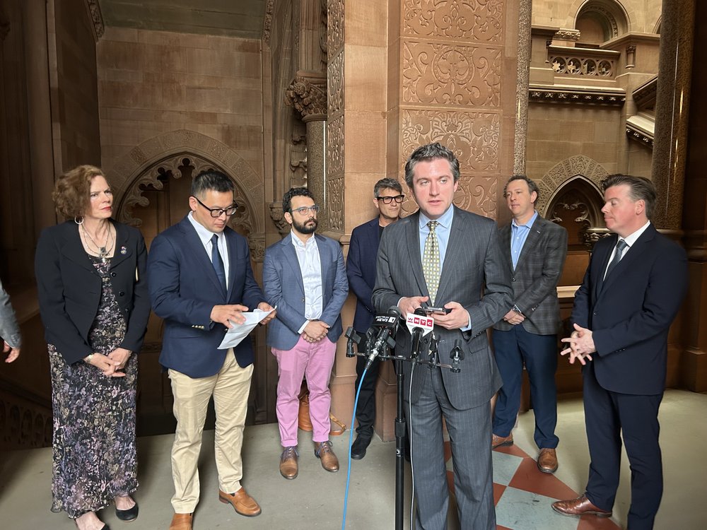 A politician speaks at a mic, flanked by supporters.