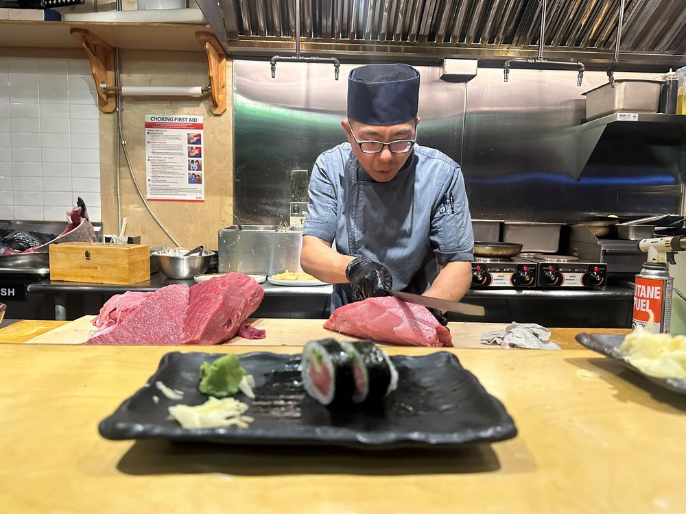 A chef carves tuna and assembles sushi.