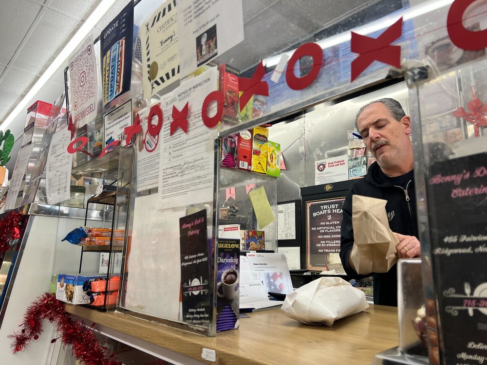 A man serves a sandwich in a bag from behind a counter.