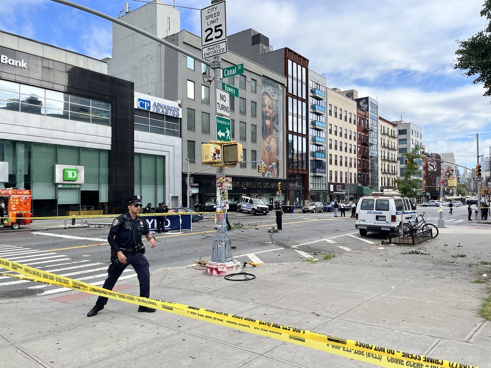 A police officer stands at attention behind a line of yellow tape surrounding a scene of a fatal crash at Canal Street and the Bowery.