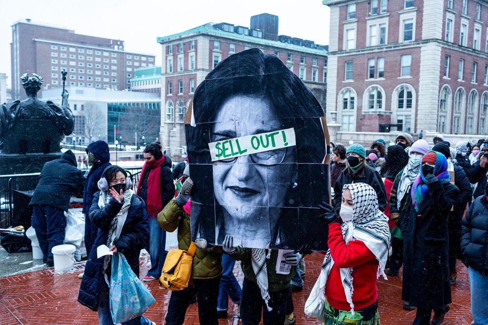 Protesters at Columbia University hold up a picture of the college's president with the words "Sell Out" over her eyes.
