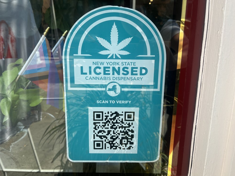 A turquoise sign posted on a window of a state-approved marijuana dispensary contains a QR code that tells customers that the store is licensed.