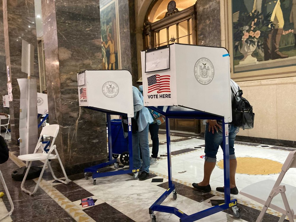 Voters behind voting privacy booths, with a mural behind them