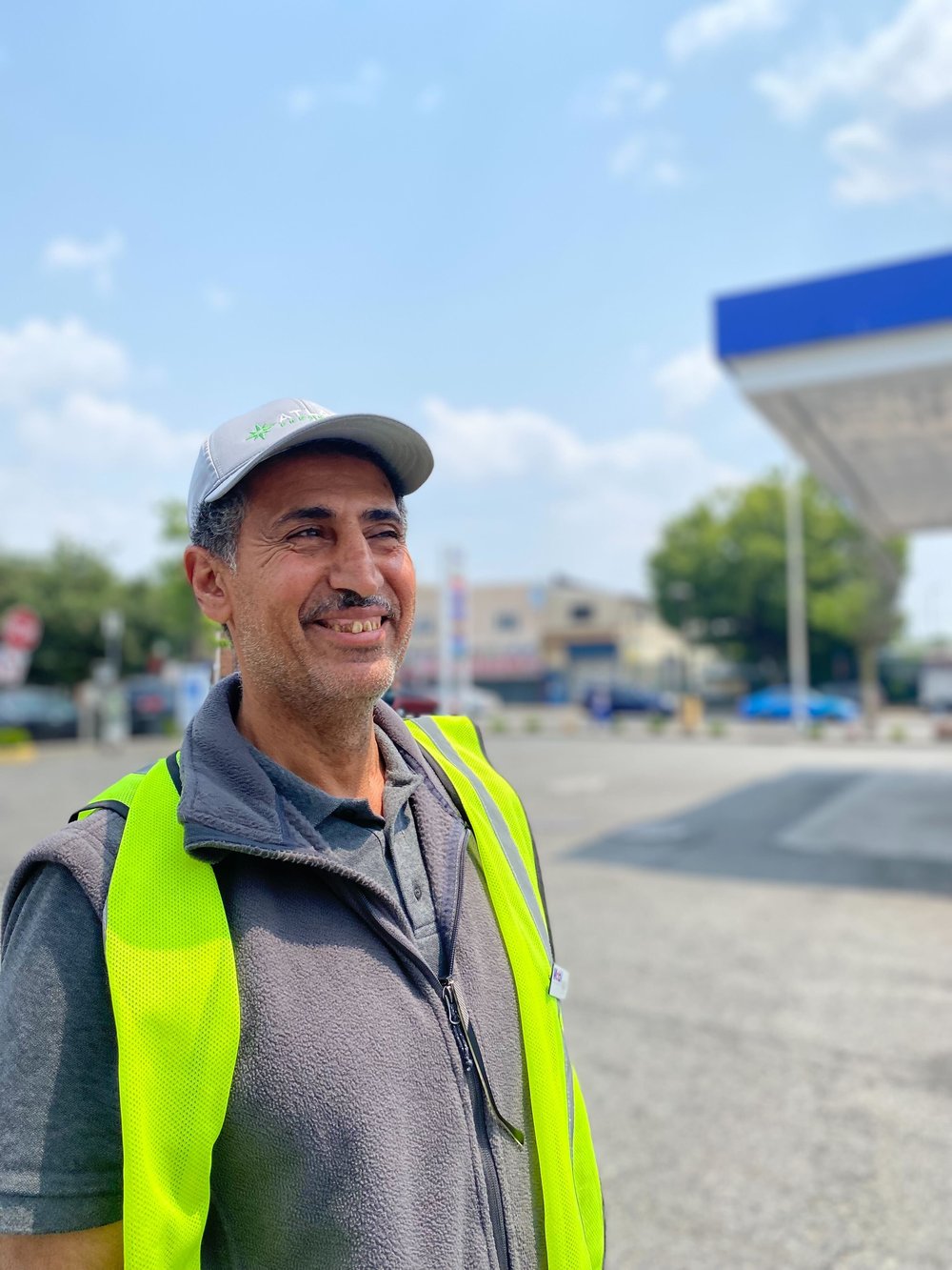 Fuad Qissi, a gas attendant at a Mobile in Newark, smiles while he's wearing a bright yellow vest.
