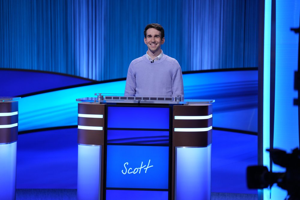 A man stands behind a blue podium with a blue curtain.