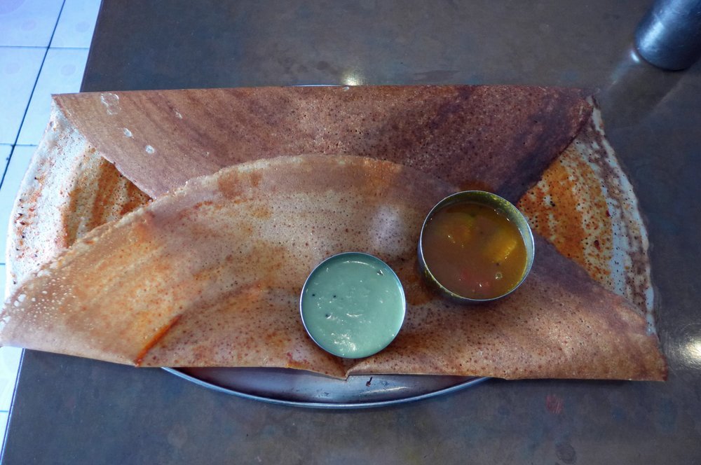A crepe-like food item, a dosa, folded over itself on a black plate.