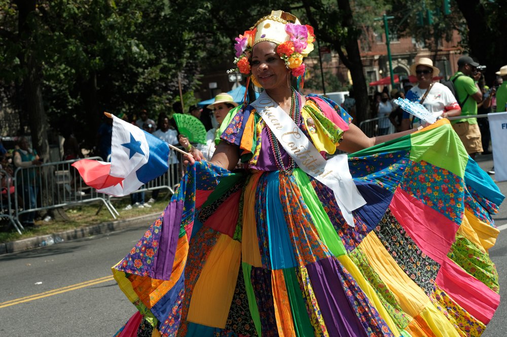 A woman in a colorful costume holds a Panamanian flag.
