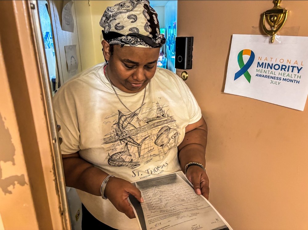 A woman standing in the door of her apartment looks at a document .