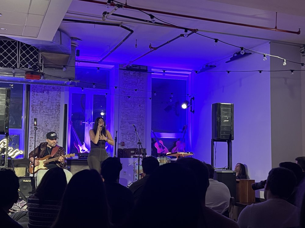 A group of people sit in a room watching a singer illuminated by blue glows.