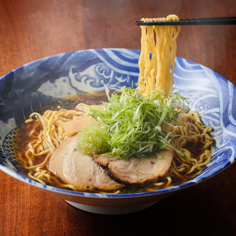 A bowl of ramen with the noodles lifted up by chopsticks