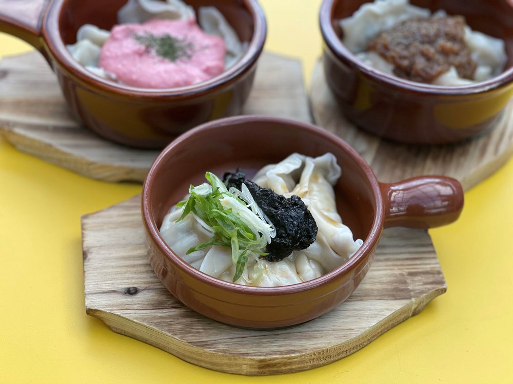 Three small bowls with dumplings covered in sauce.
