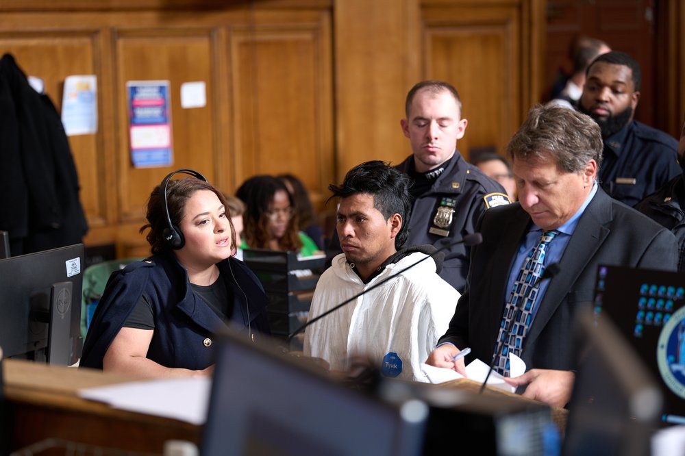 A man in white is surrounded by police and an attorney in a courtroom.
