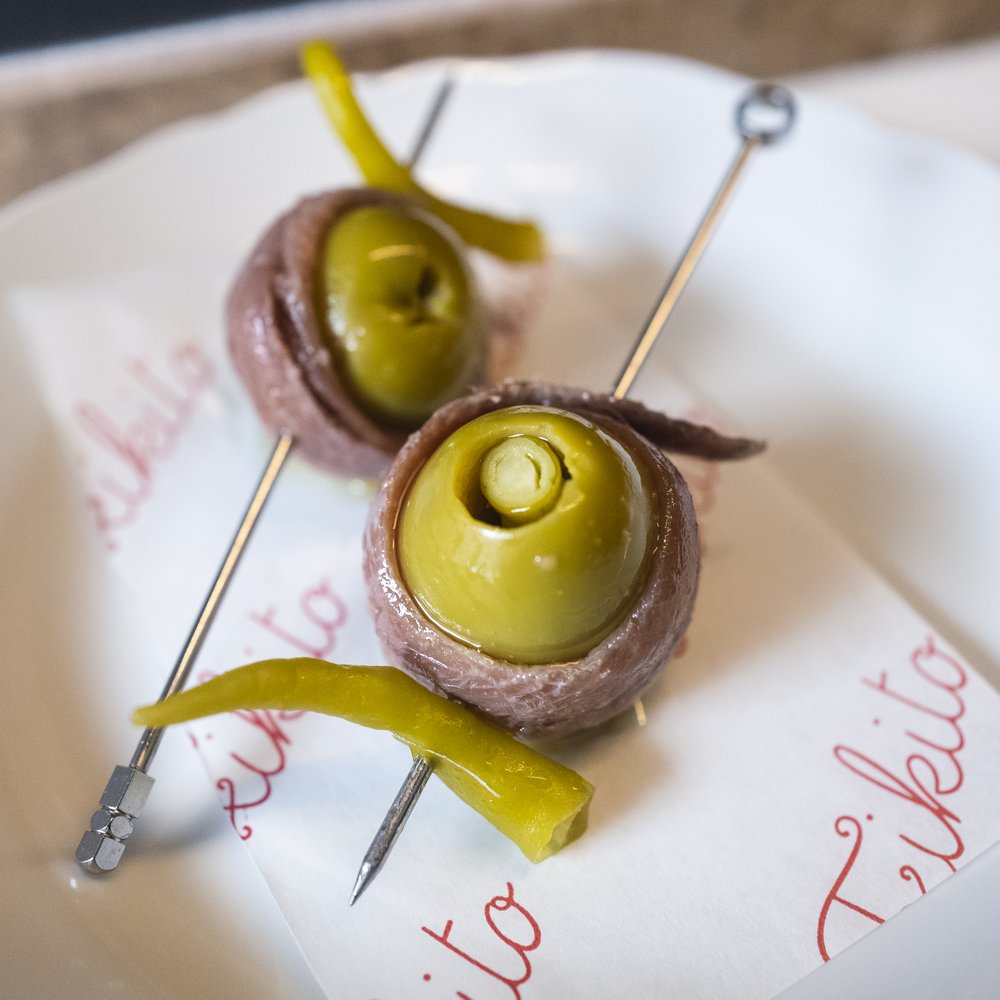 Two skewers that feature large olives wrapped in anchovy.