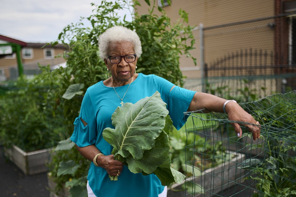 A gardener poses for a picture holding a large leaf across their chest.