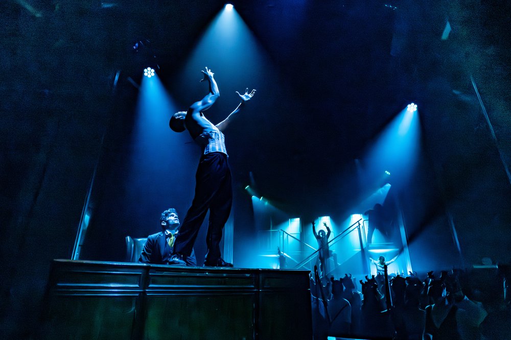 Actors on a stage under blue lights.
