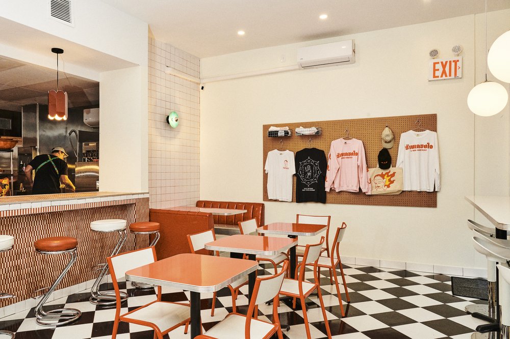The space, a former Chinese take-out spot, is small, with a six-seat counter, a few tables, and a gleaming glittering red-vinyl booth in the corner. An open kitchen and a wall full of merch, designed by Aiemsaard, complete the space.