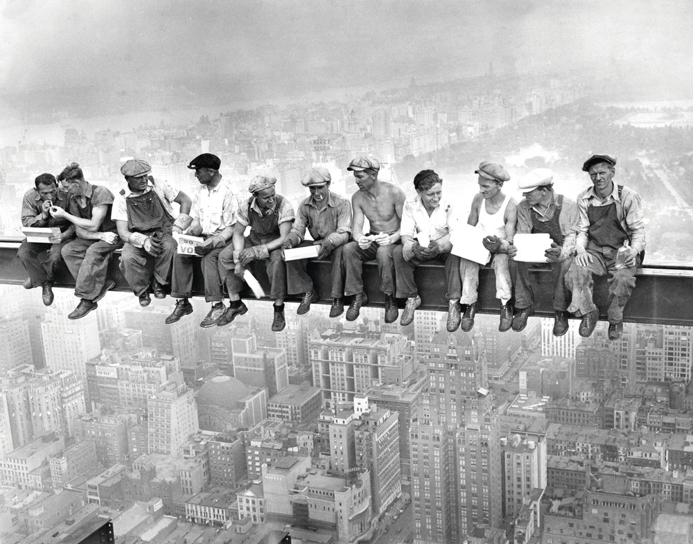 A group of construction workers on a beam in a black and white photo