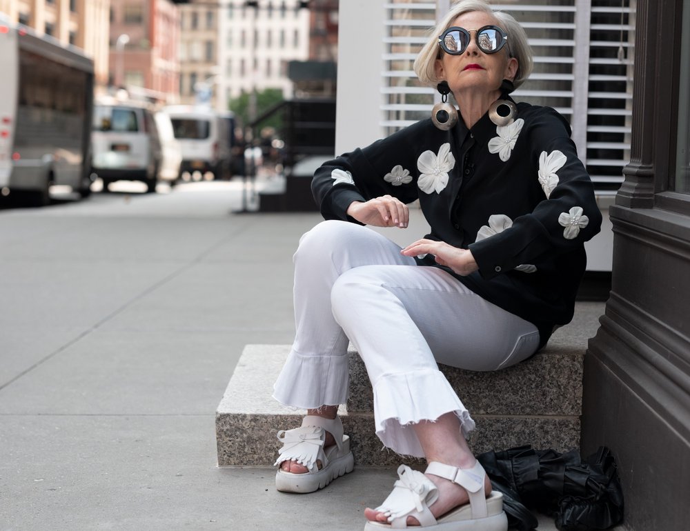 A woman wearing black and white sits on steps in a city.