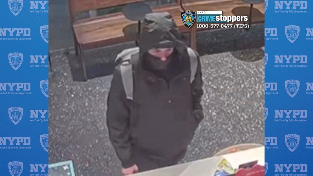 A man with a face mask and a dark jacket stands at a counter.