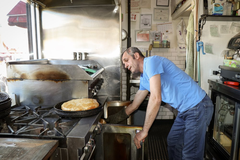 A man in a blue T-shirt and jeans reaches into an oven.